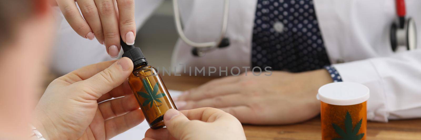 Close-up of doctor give bottle with extract oil of cannabis for health treatment. Man on appointment in clinic. Alternative medicine, healthcare concept