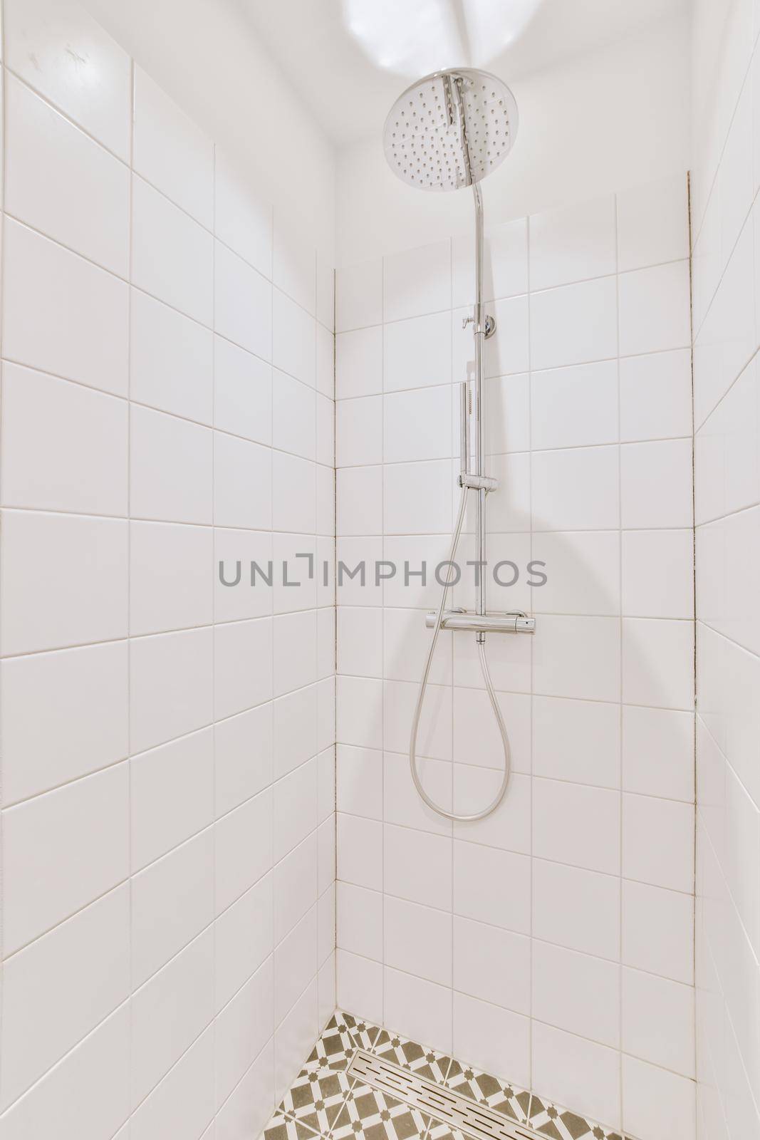 Shower faucets attached to tiled wall near glass partition and ornamental curtail in washroom at home