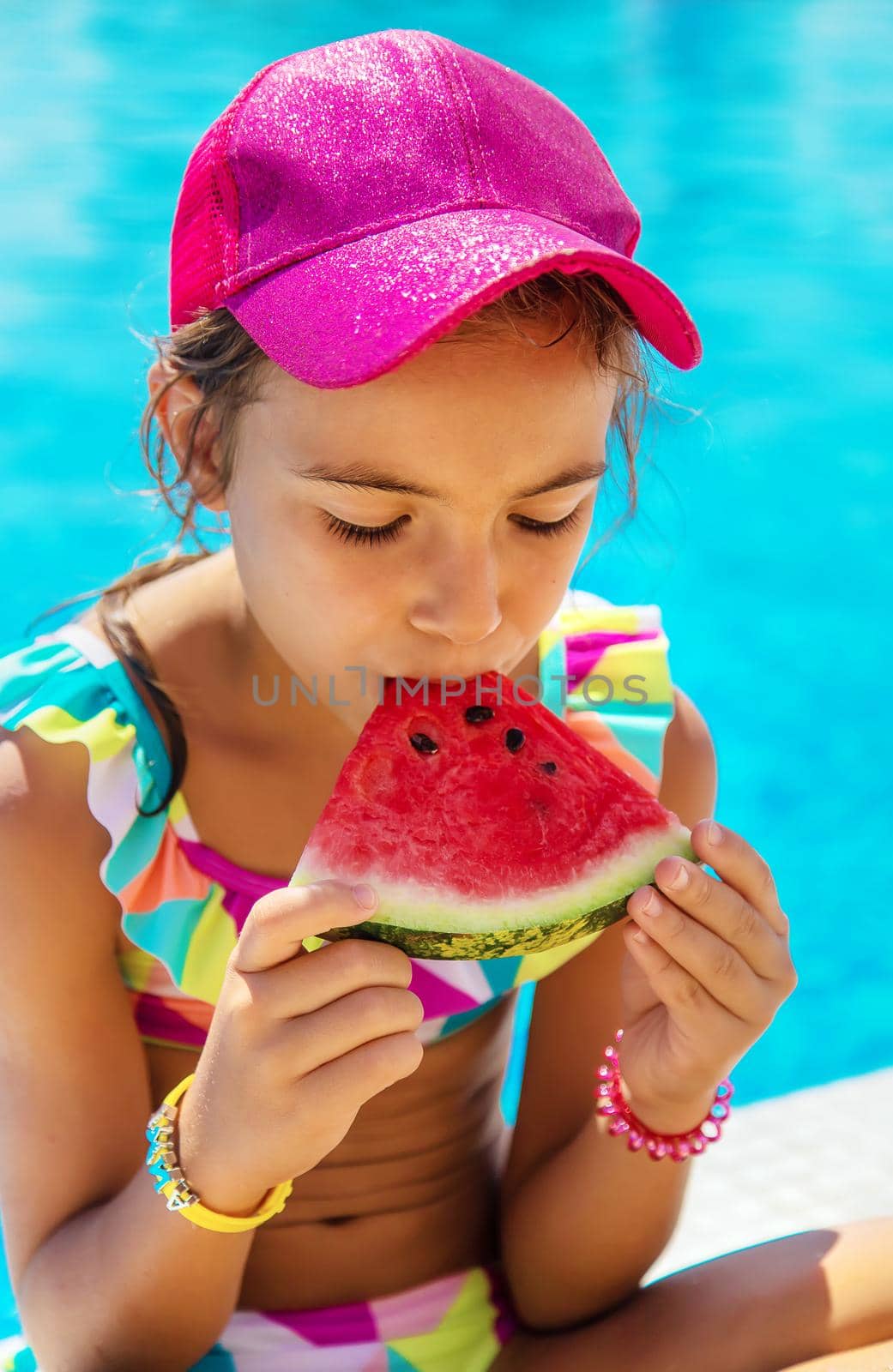 The child eats a watermelon near the pool. Selective focus. Kid.