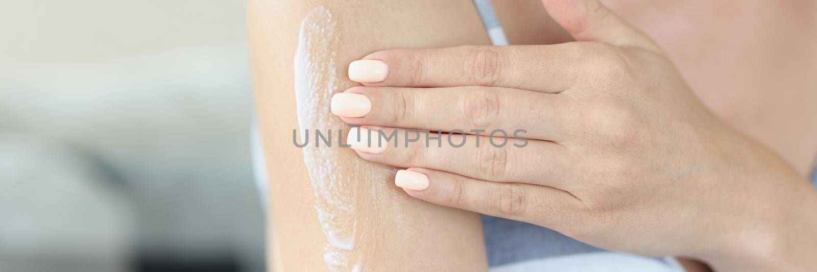 Close-up of young woman applying gently moisturizing body lotion on arm. Take care of her skin condition after shower or bath. Wellness, beauty concept