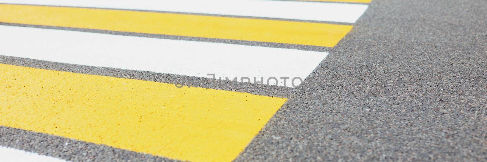 Close-up of marked white and yellow walkway across road or street. Crosswalk or pedestrian crossing. Simply painted lines on asphalt for crossing street safety