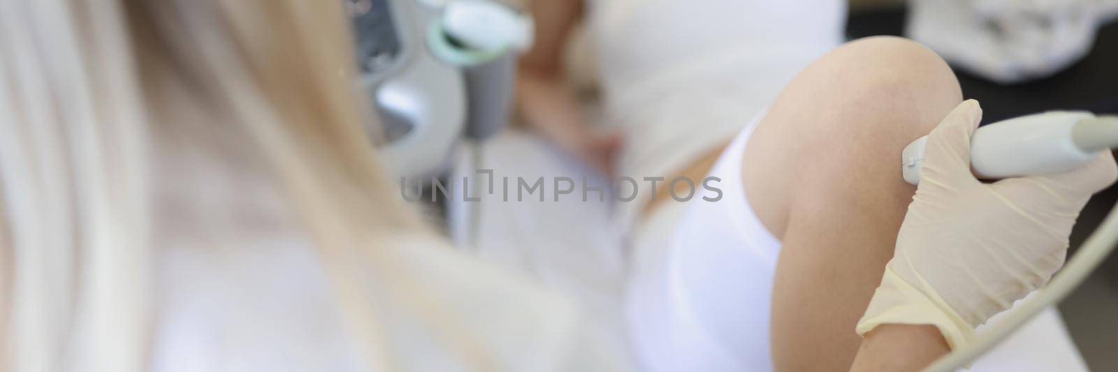 Female doctor conducting ultrasound examination of patients knee in clinic by kuprevich