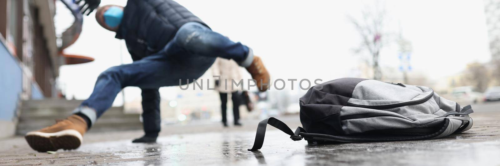 Low angle of male person get injury after falling on slippery ground in winter. Personal bag lay on asphalt ice. Accident, trauma, fracture, clumsy concept