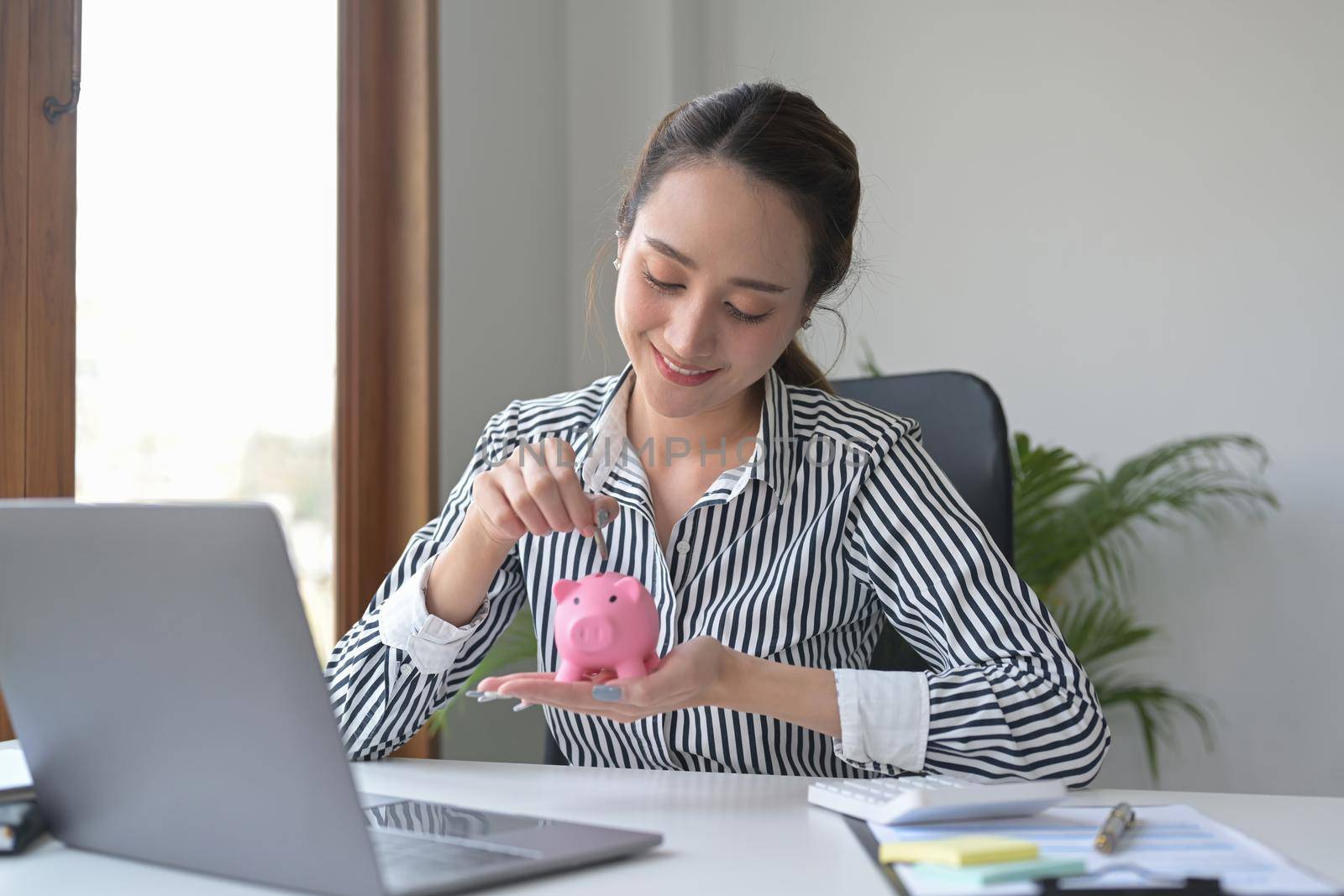 Attractive young woman putting coin into piggy bank. Saving money, banking, economy concept.