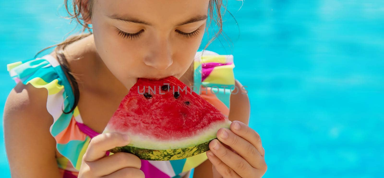 The child eats a watermelon near the pool. Selective focus. Kid.