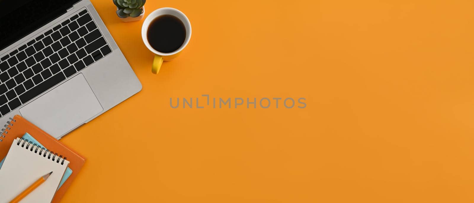 Computer laptop, coffee cup and notebook on yellow background with copy space. Horizontal photo, Top view.