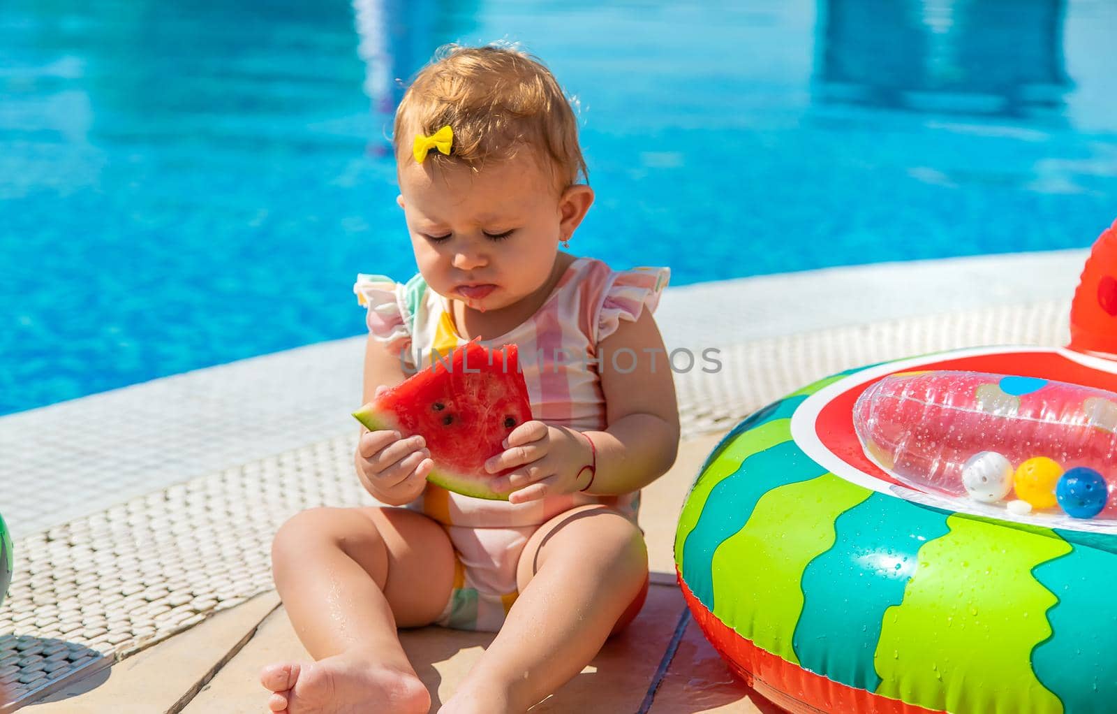 Baby is eating a watermelon by the pool. Selective focus. Kids.