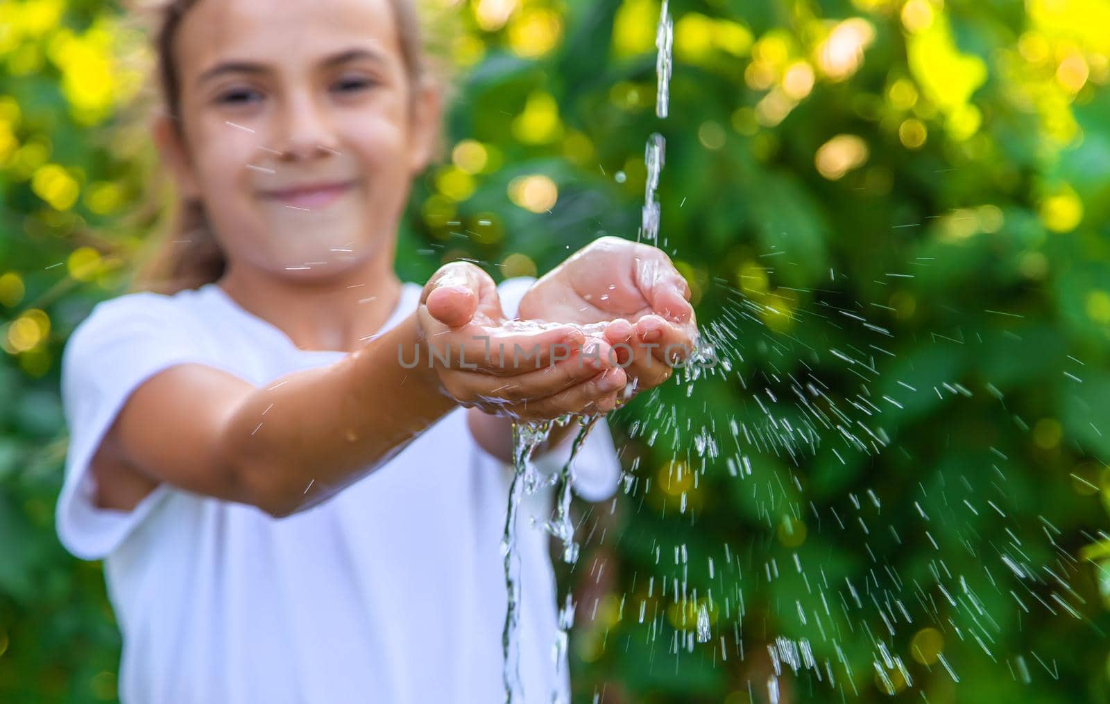 The water flows into the hands of the child. Selective focus. Nature.