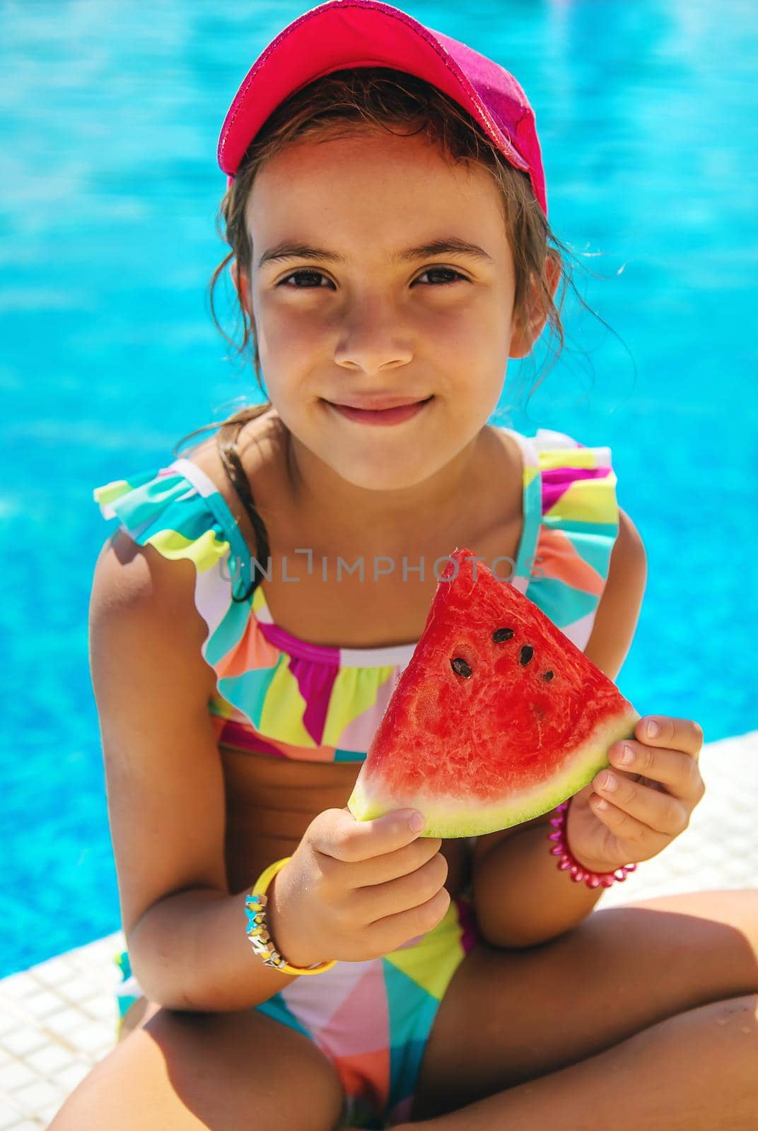The child eats a watermelon near the pool. Selective focus. Kid.