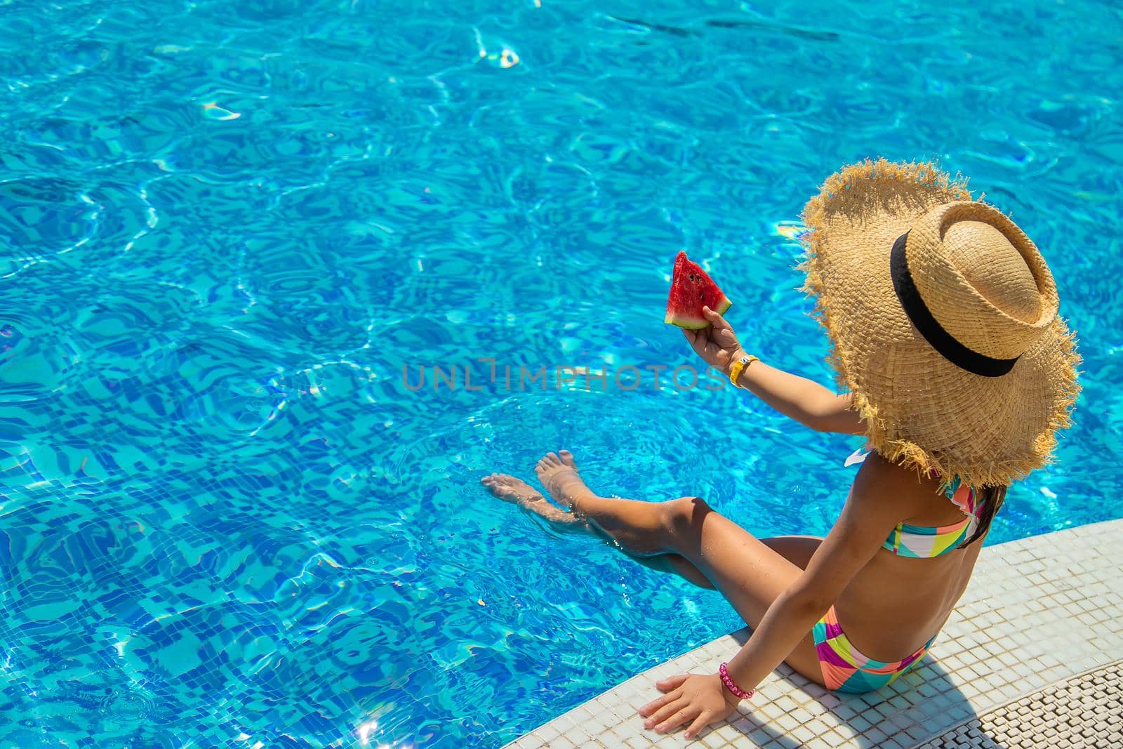 The child eats a watermelon near the pool. Selective focus. Kid.