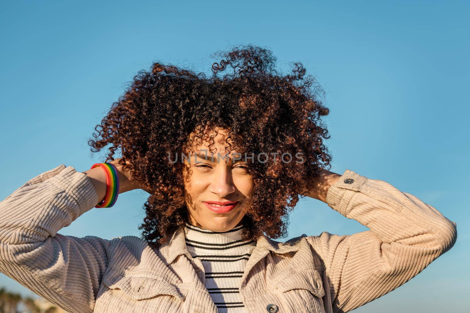 portrait of a beautiful young black woman with a rainbow bracelet smiling and playing with her curly afro hair, concept of beauty, youth and diversity, copy space for text