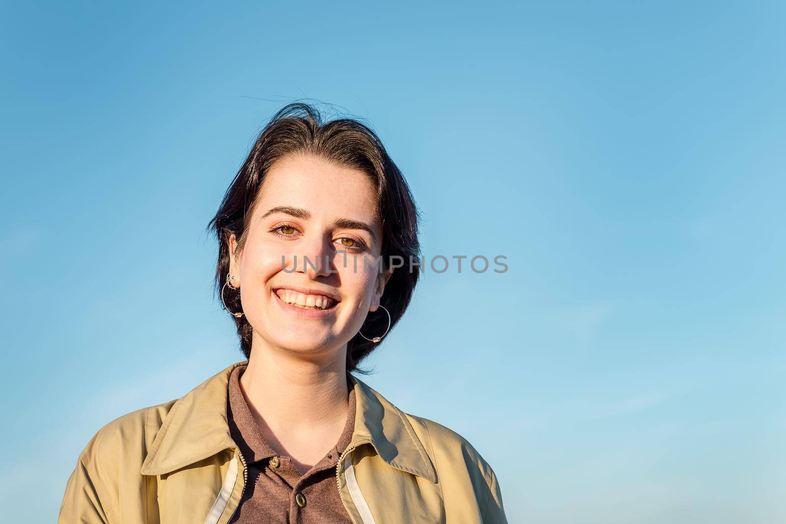 portrait of a young pretty woman with short hair and beautiful green eyes smiling in front of a blue sky background, concept of beauty, youth and diversity, copy space for text