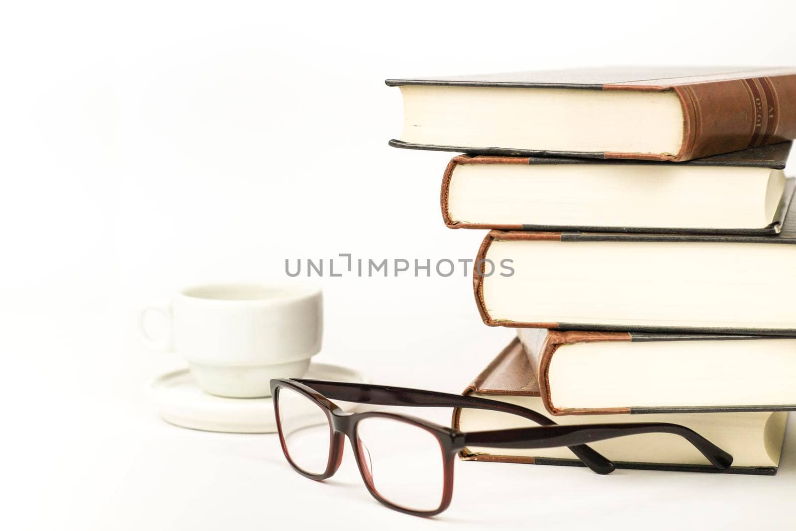 Stacked books next to cup of coffee and eyeglasses on white background