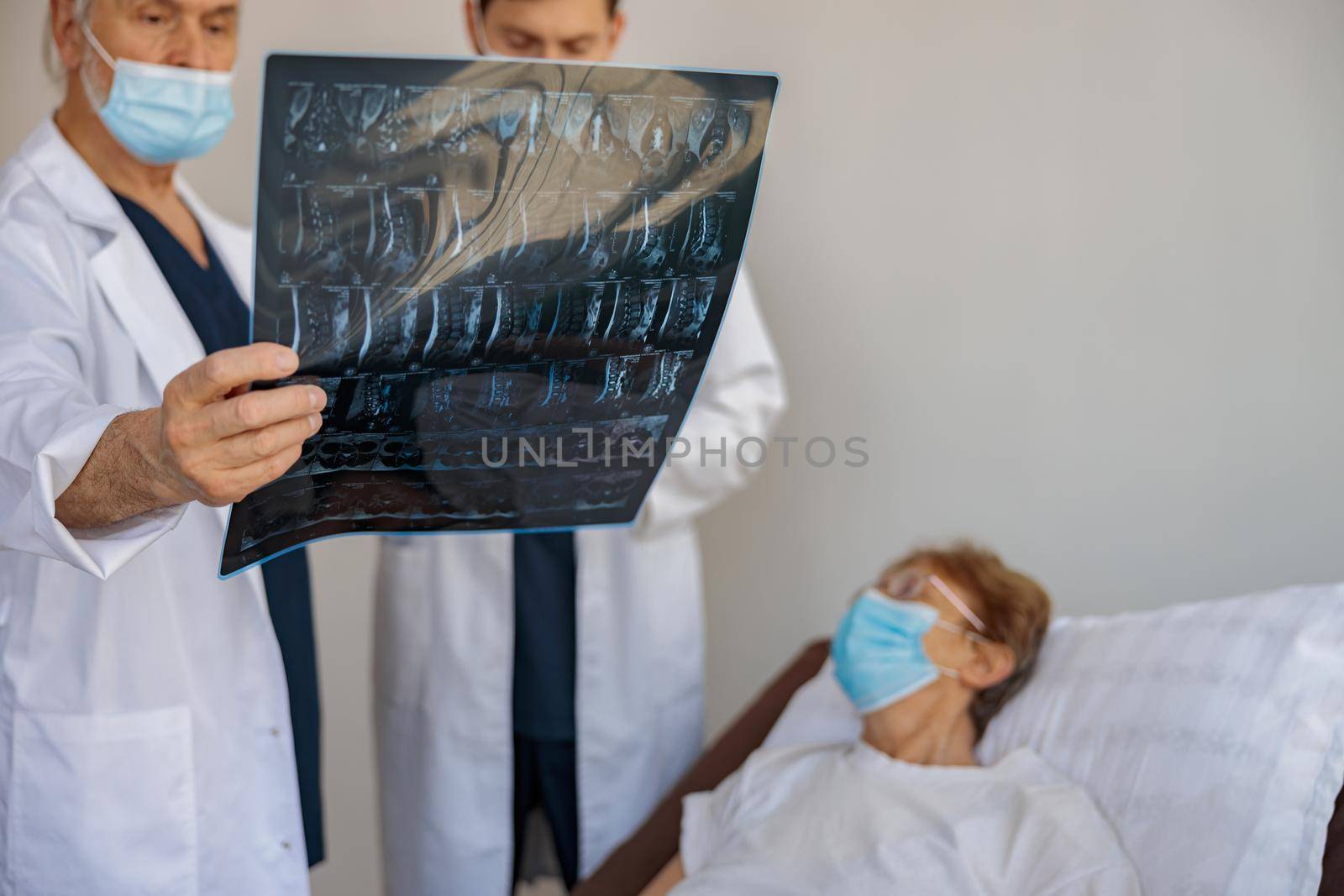 Two doctors in mask look and discuss an X-ray or MRI scan of the patient in clinic by Yaroslav_astakhov