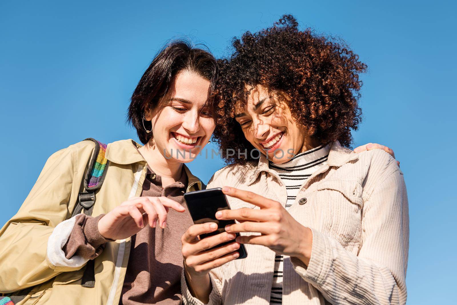 multiracial couple of young women enjoying funny while looking at the phone, concept of technology and racial diversity