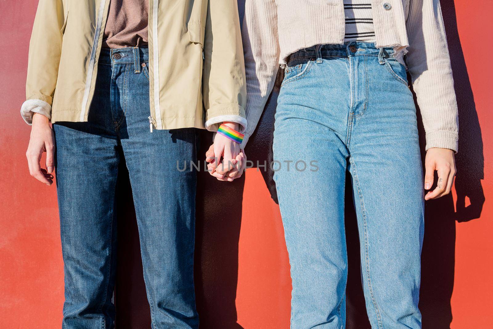 detail of two women linking hands with a bracelet in the colors of the rainbow flag, symbol of the struggle for homosexual rights, concept of sexual freedom and diversity