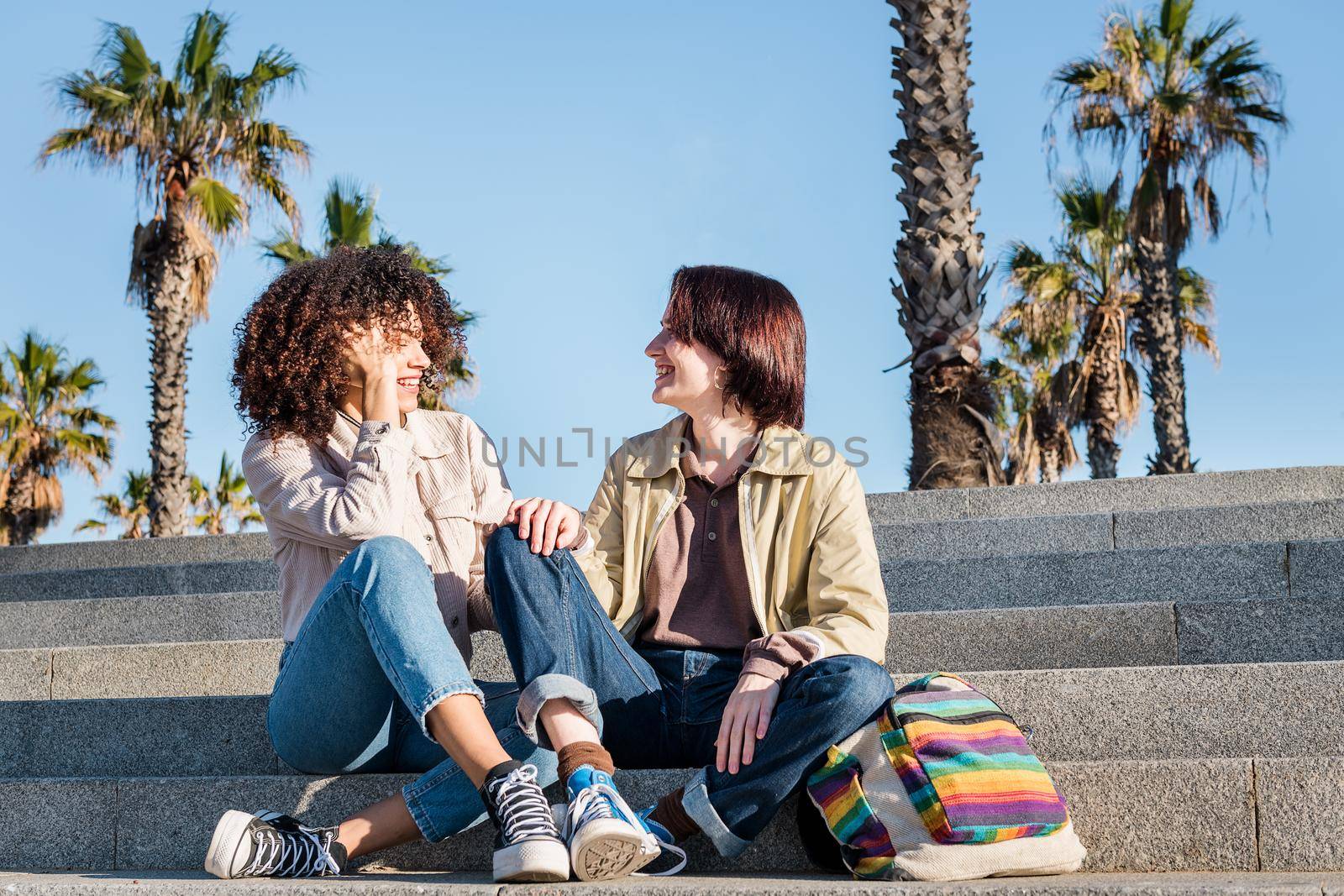 young interracial couple of gay women chatting on the stairs, concept of sexual freedom and racial diversity