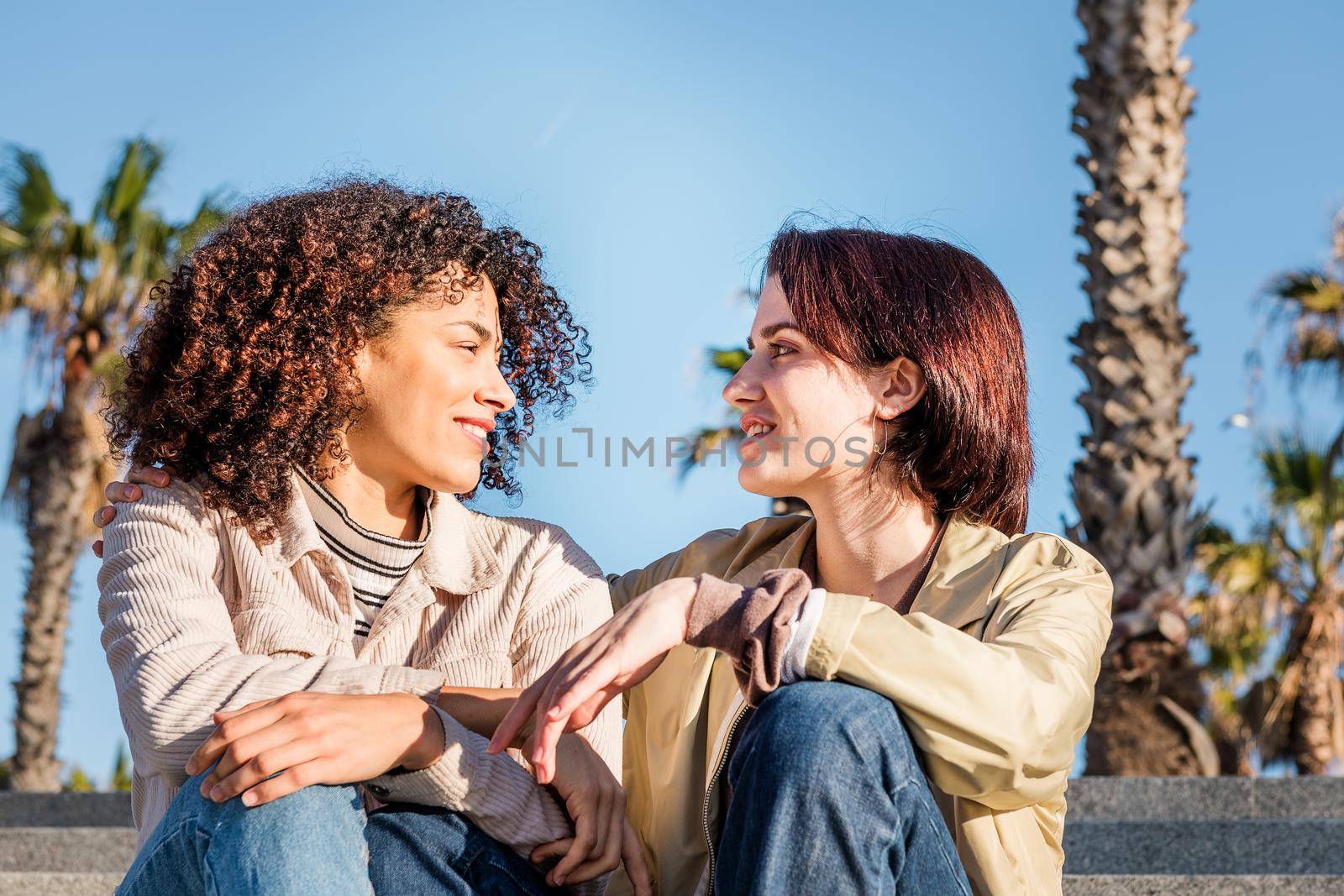 young interracial couple of homosexual women talking sitting on the stairs, concept of sexual freedom and racial diversity