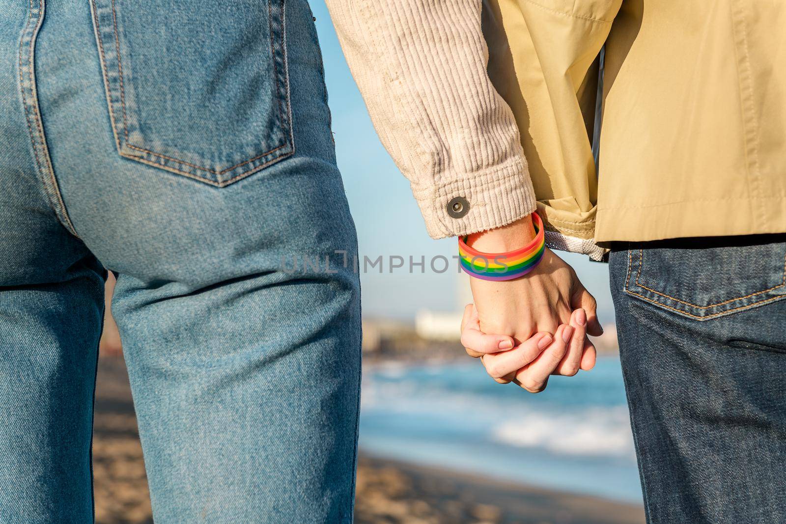 detail of the linked hands of two gay women with a rainbow flag bracelet, symbol of the struggle for homosexual rights, concept of sexual freedom and diversity