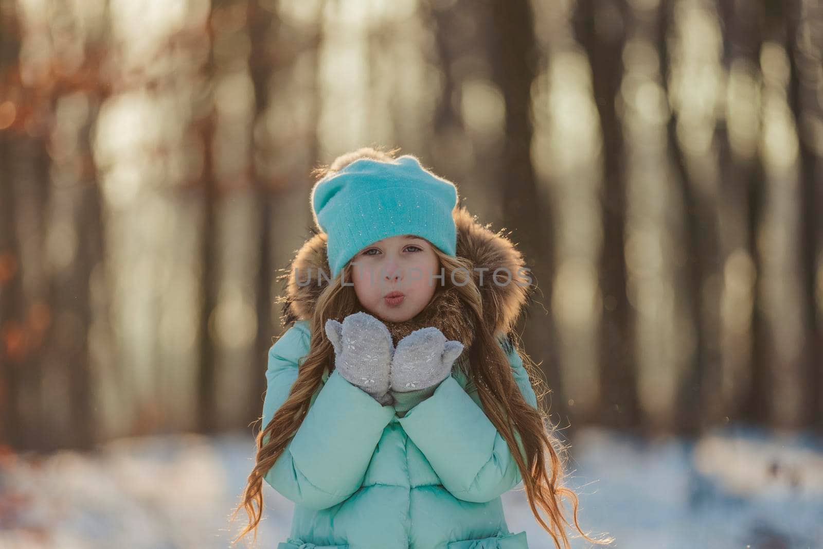 little girl blows on the snow that is on her mittens