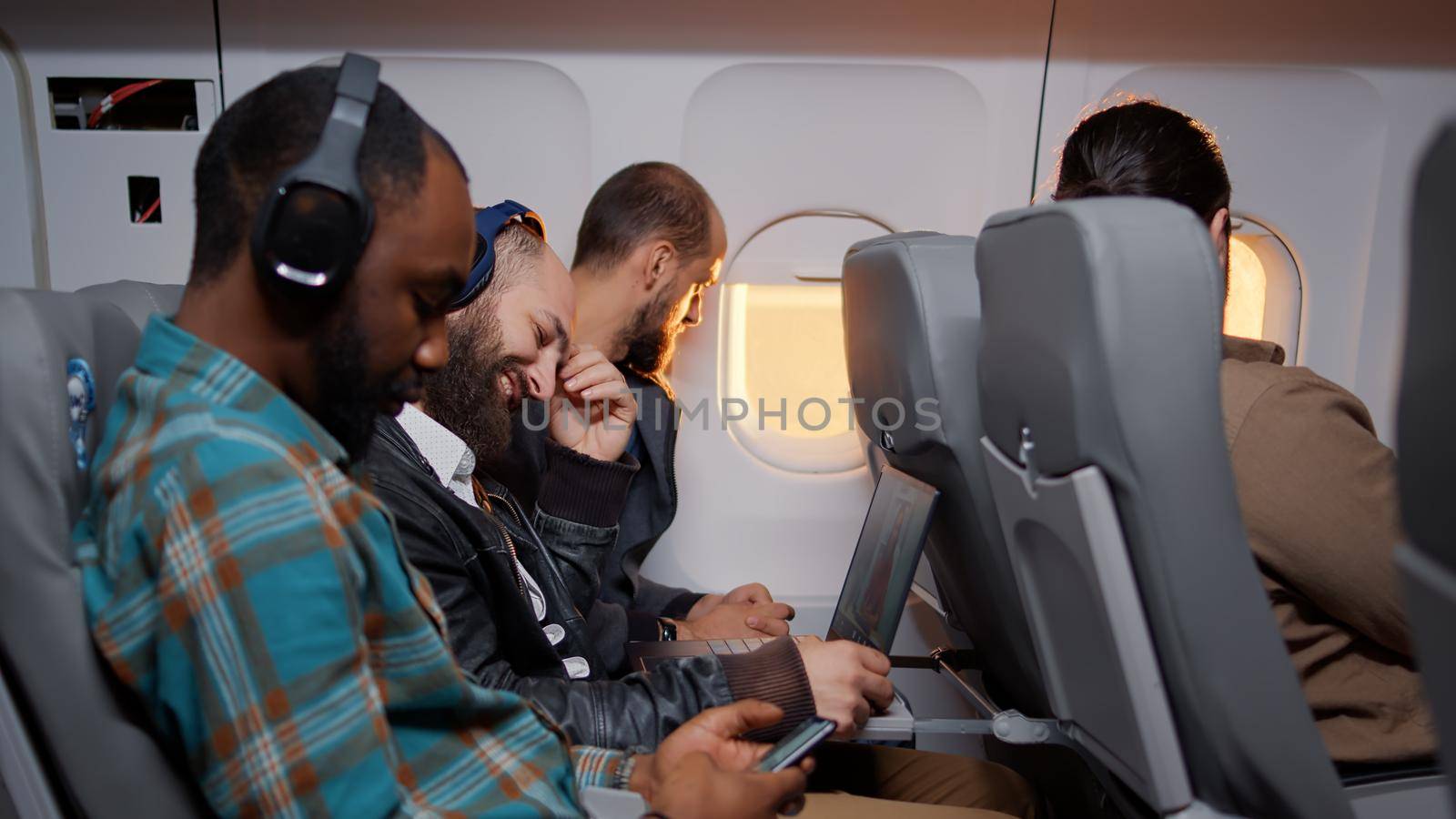 Group of male tourists travelling by airplane during sunset, flying with international airline jet on vacation. Flying in economy class with passengers on aviation service.