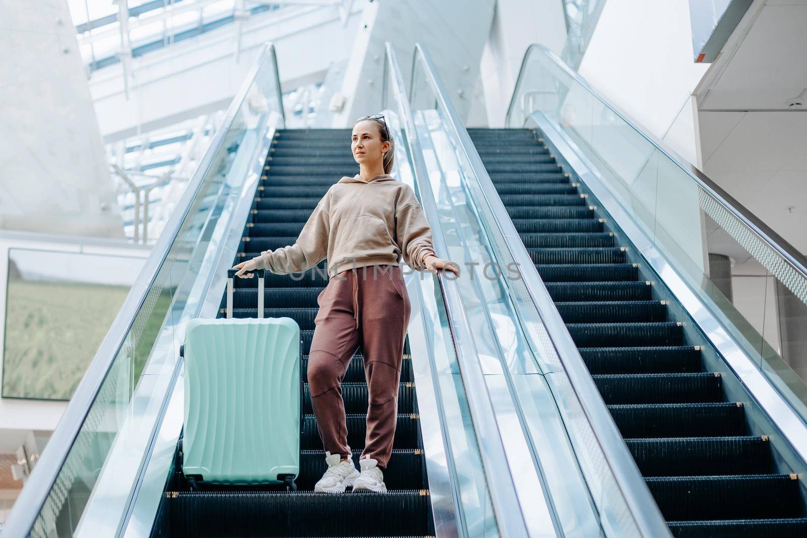 young woman with luggage standing on the escalator at the airport. by SmartPhotoLab