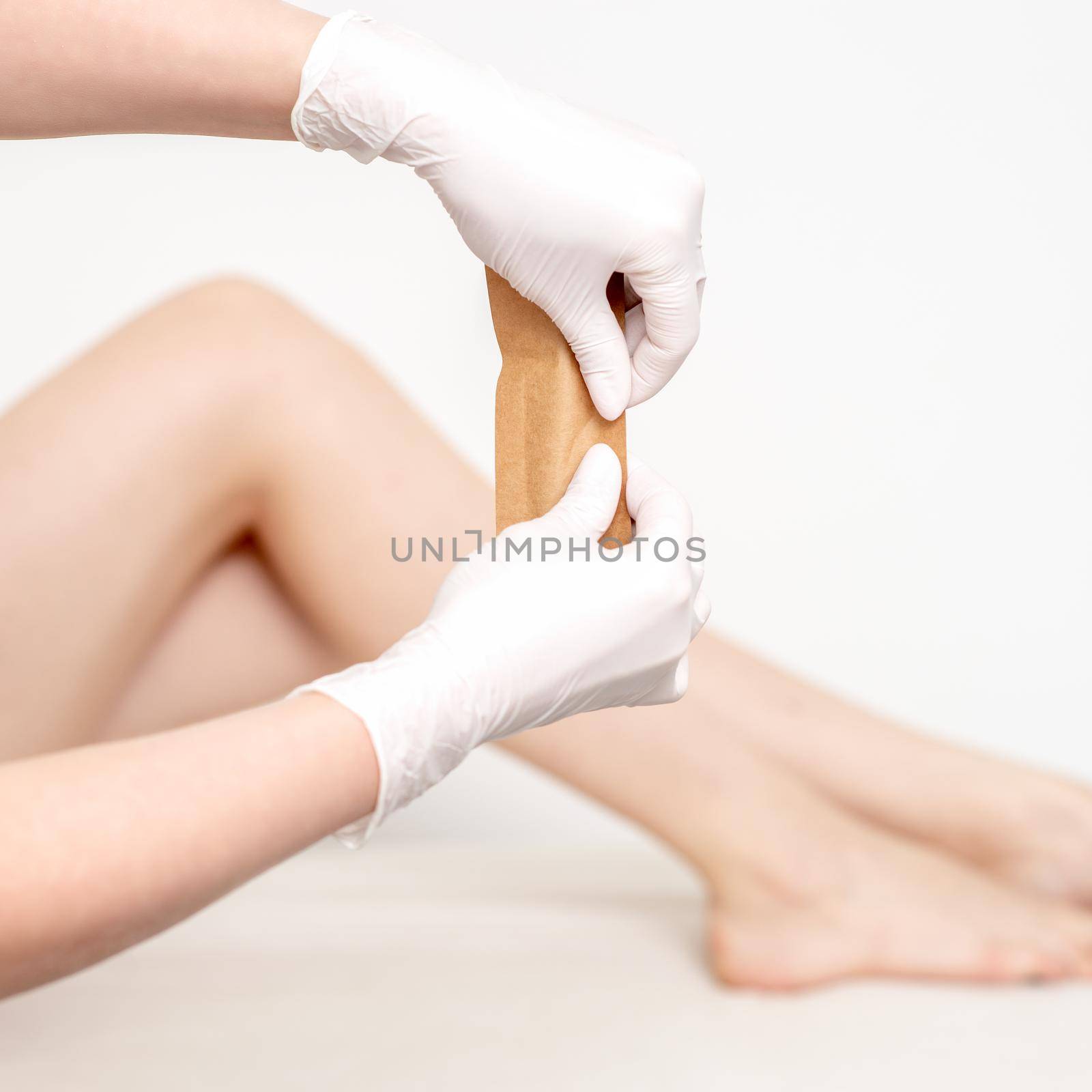 Human hands in protective gloves holding craft envelope with medical or beauty tools on background of female legs