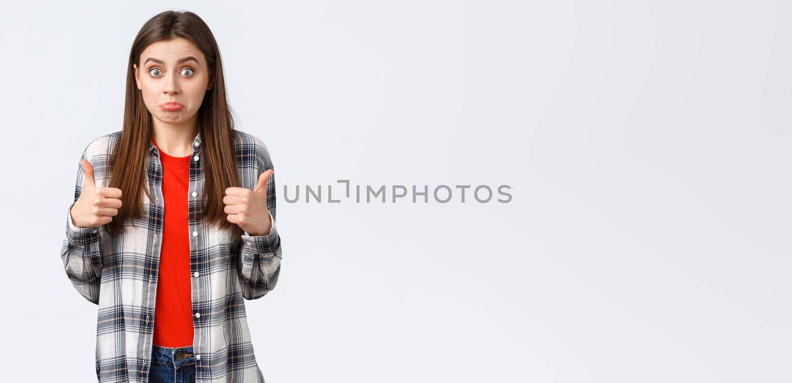 Lifestyle, different emotions, leisure activities concept. Not bad I guess. Cute girl surprised with positive result, show thumb-up and make confused expression, standing white background.