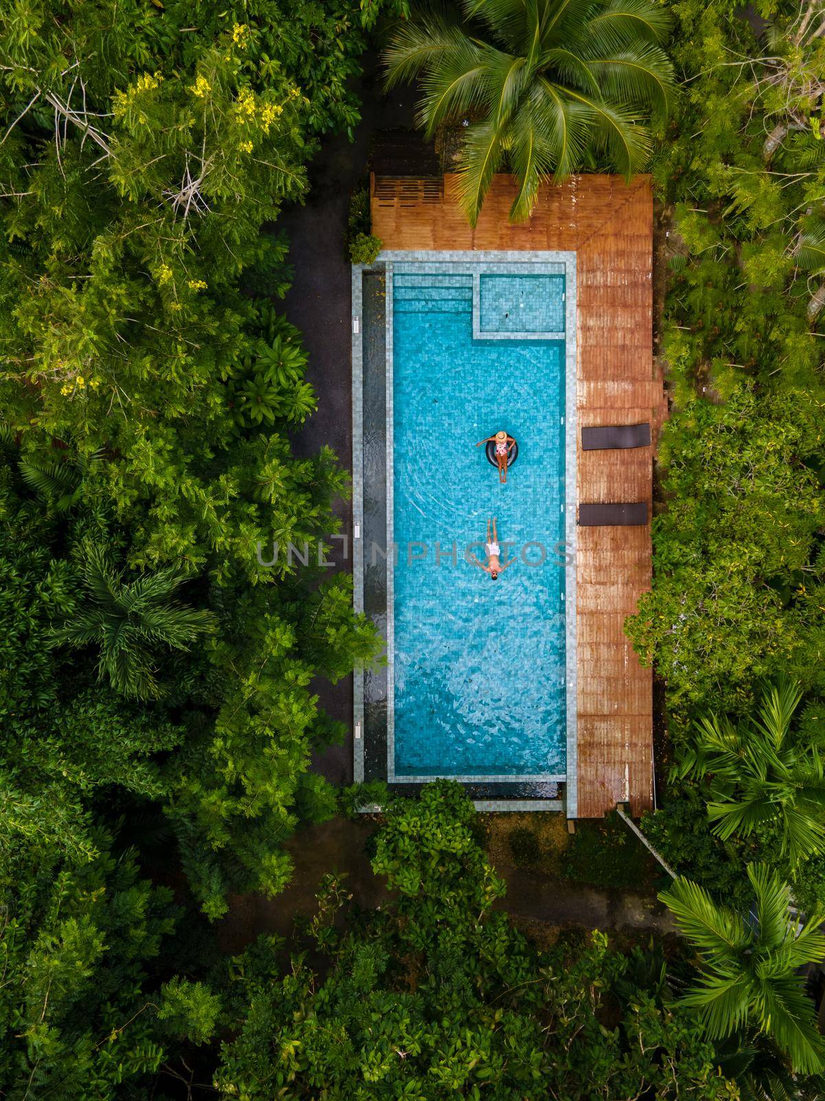 couple men and woman in swimming pool in the jungle of Krabi Thailand, aerial view with drone above swimming pool in jungle of Thailand by fokkebok
