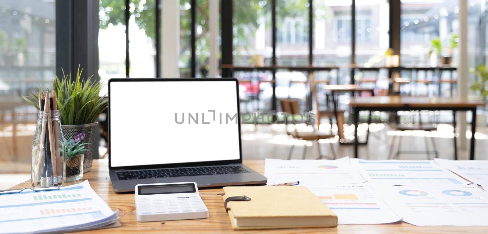 Laptop or notebook with blank screen on wood table in blurry background with house or office modern ,nature orange bokeh and sunlight in morning..