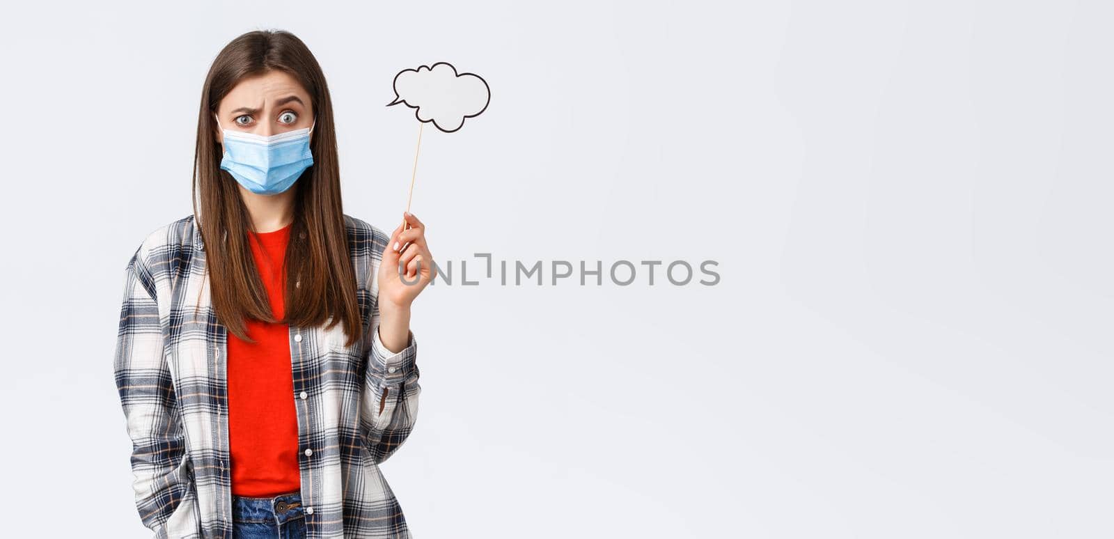 Coronavirus outbreak, leisure on quarantine, social distancing and emotions concept. Confused and clueless young girl in medical mask have no ideas, hold cloud stick near head.