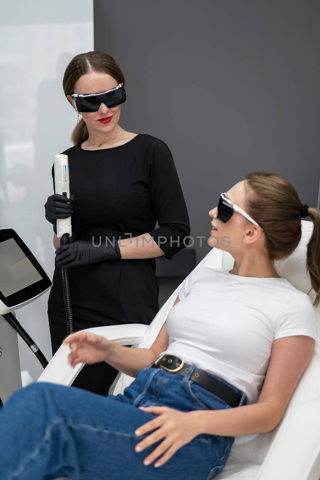 A woman on a couch in goggles undergoing a photorejuvenation procedure. Cosmetologist with a patient. by mrwed54