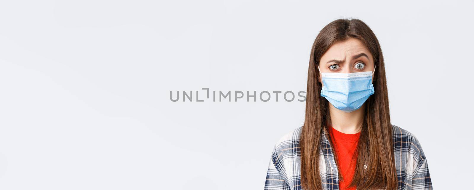 Coronavirus outbreak, leisure on quarantine, social distancing and emotions concept. Confused young woman cant understand what happening, look suspicious or surprised, wear medical mask by Benzoix