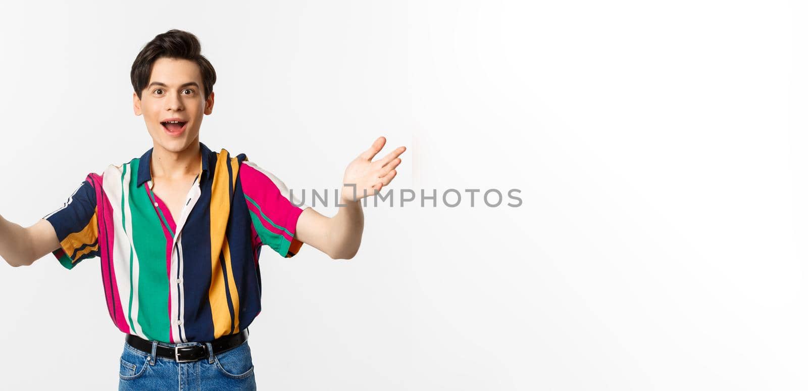 Amazed young handsome man reaching hands forward, want to hold or take something, looking with desire, standing over white background.