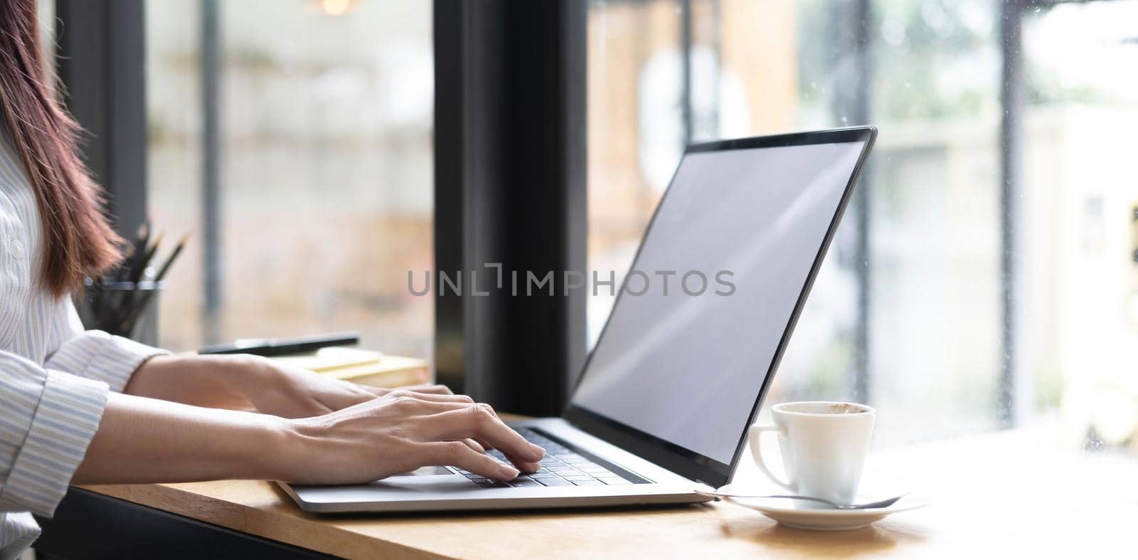 Businesswoman's handis typing a keyboard on a laptop with a blank white screen. Close-up of woman's hands working on desk. by wichayada