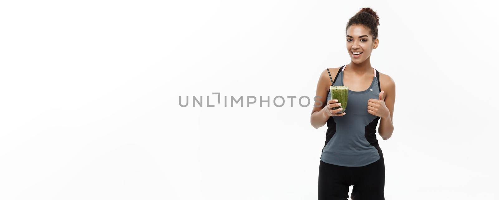 Healthy and Fitness concept - Beautiful American African lady in fitness clothing drinking healthy vegetable drink. Isolated on white background. by Benzoix