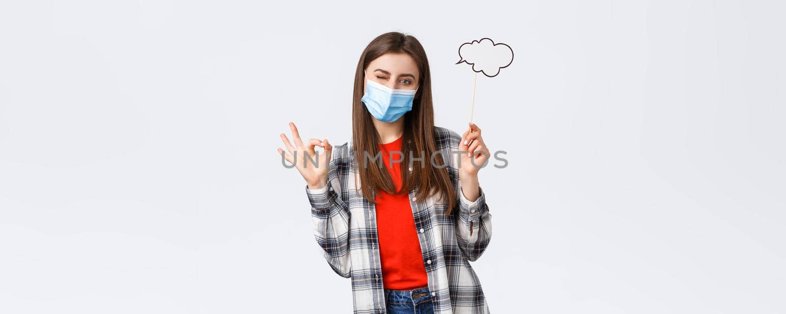 Coronavirus outbreak, leisure on quarantine, social distancing and emotions concept. No problem, girl have good idea, wink assuring and show okay sign, wear medical mask, hold commend bubble.