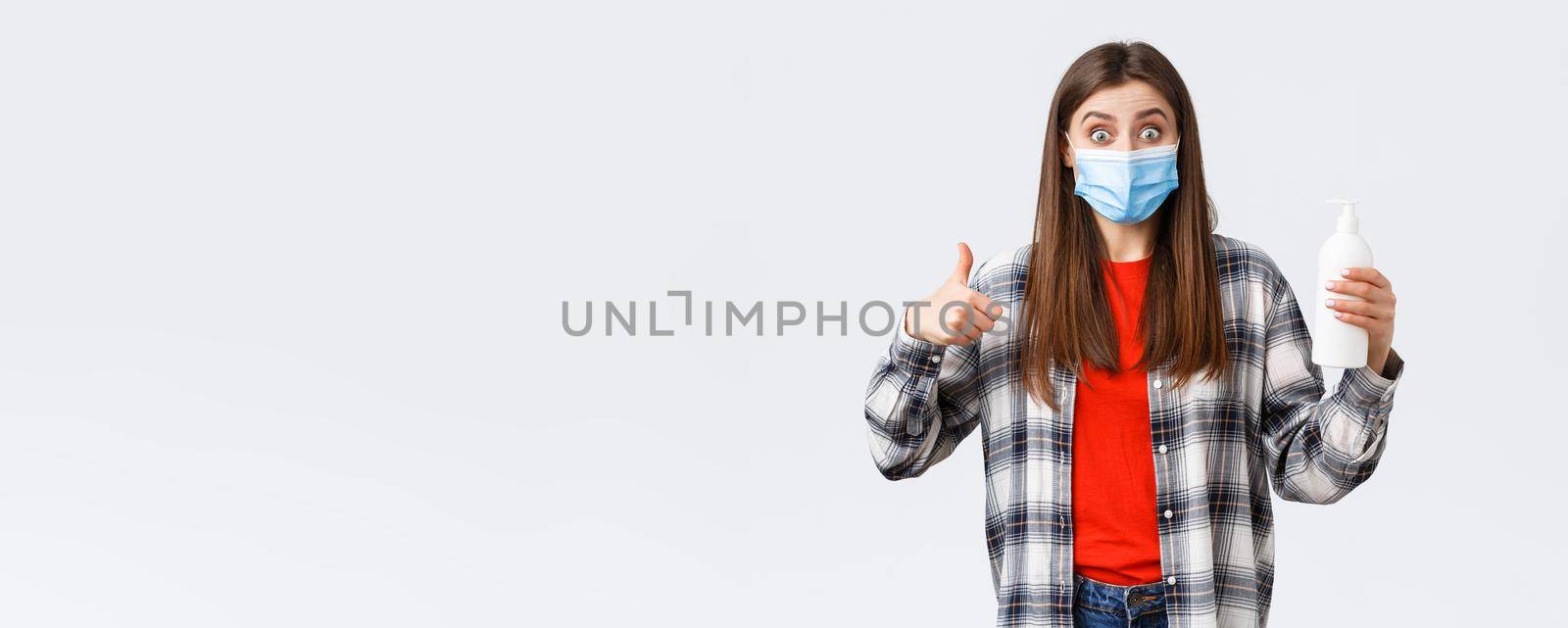 Coronavirus outbreak, leisure on quarantine, social distancing and emotions concept. Excited and satisfied girl in medical mask promote great hand sanitizer, preventing virus soap, thumb-up by Benzoix