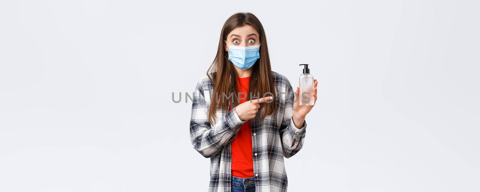 Coronavirus outbreak, leisure on quarantine, social distancing and emotions concept. Excited and astonished young woman in medical mask, pointing at hand sanitizer, recommend product.
