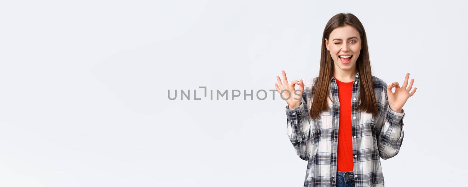 Lifestyle, different emotions, leisure activities concept. Confident and assured enthusiastic young woman in checked shirt assure all okay, promise or guarantee, show okay sign, smiling and wink by Benzoix