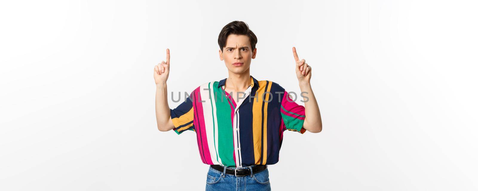 Disappointed and angry man pointing fingers up, showing something bad, standing over white background. Copy space