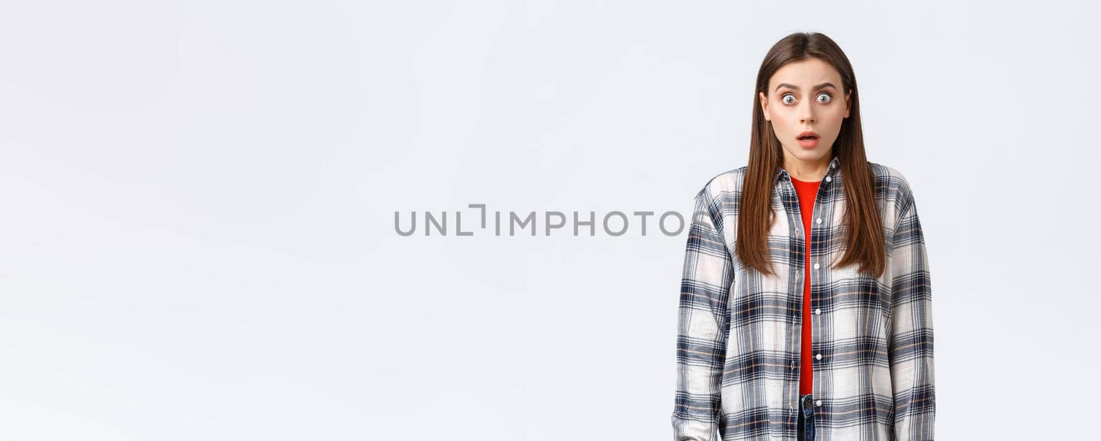 Lifestyle, different emotions, leisure activities concept. Shocked and scared, startled young woman in checked casual shirt, staring terrified, see something scary, standing in stupor by Benzoix