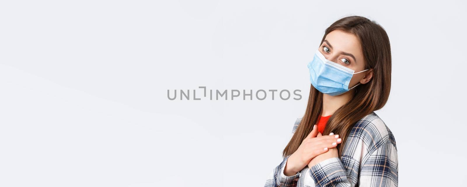 Coronavirus outbreak, leisure on quarantine, social distancing and emotions concept. Tender and touched young woman in medical mask, hold hands on heart feel grateful, white background by Benzoix