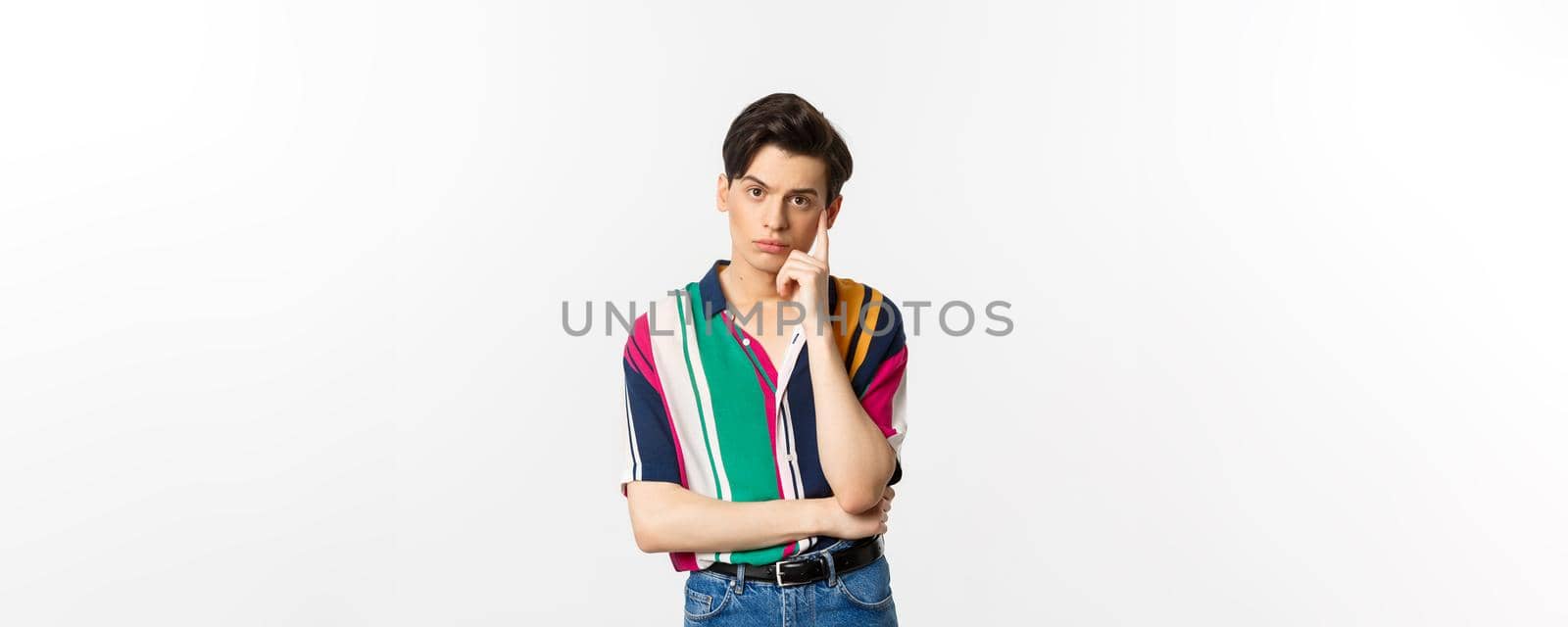 Image of attractive young man staring at camera with reluctant and annoyed emotion, standing over white background.