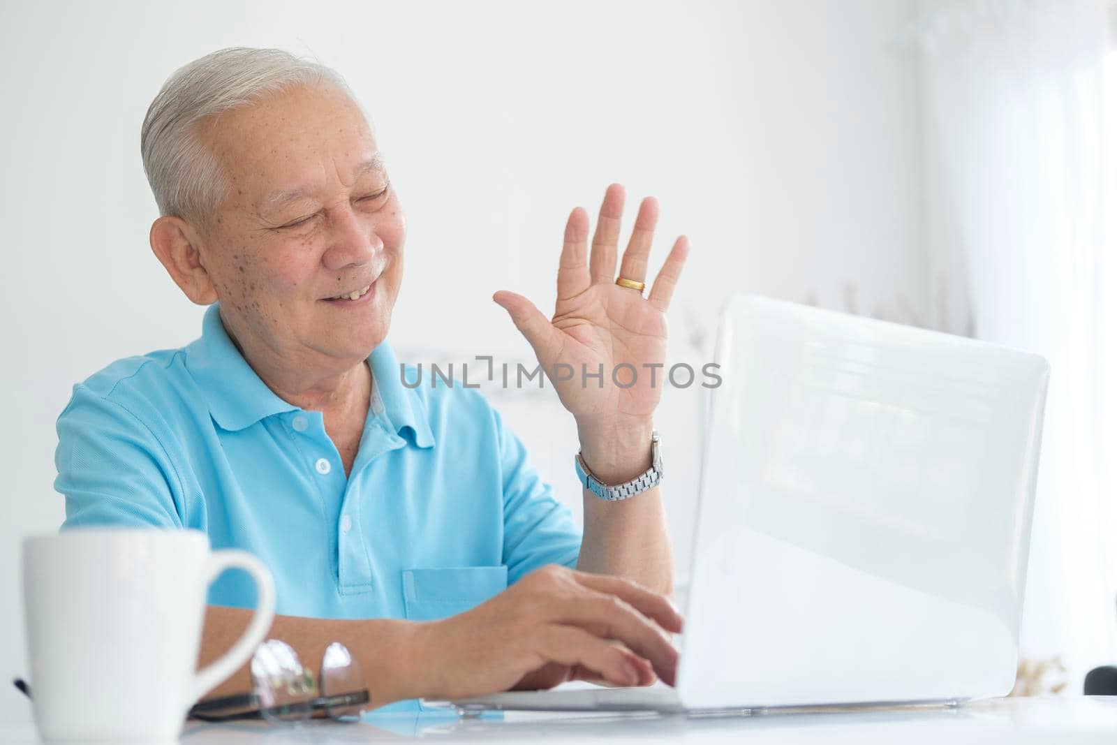 Elderly man making video call and waving at screen, chatting with children, communication with friend distantly, older generation modern tech easy comfortable usage concept..