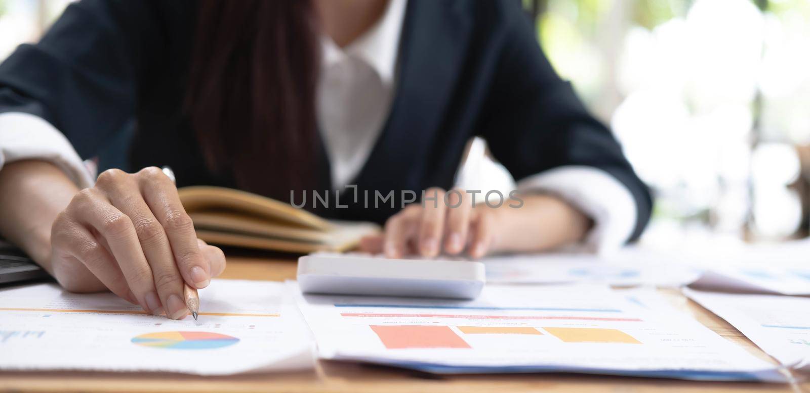 Close up of Hand business woman holding pen pointing on chart summary report and calculate finance. by wichayada