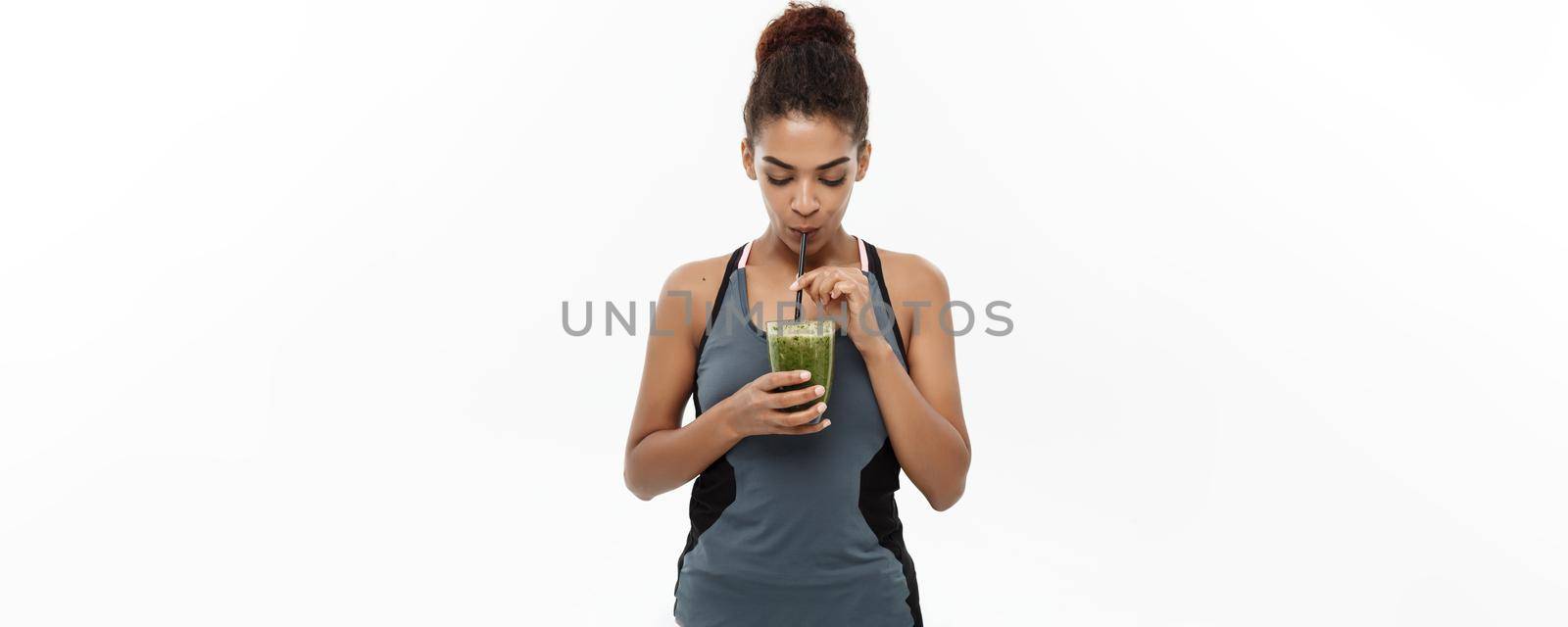 Healthy and Fitness concept - Beautiful American African lady in fitness clothing drinking healthy vegetable drink. Isolated on white background