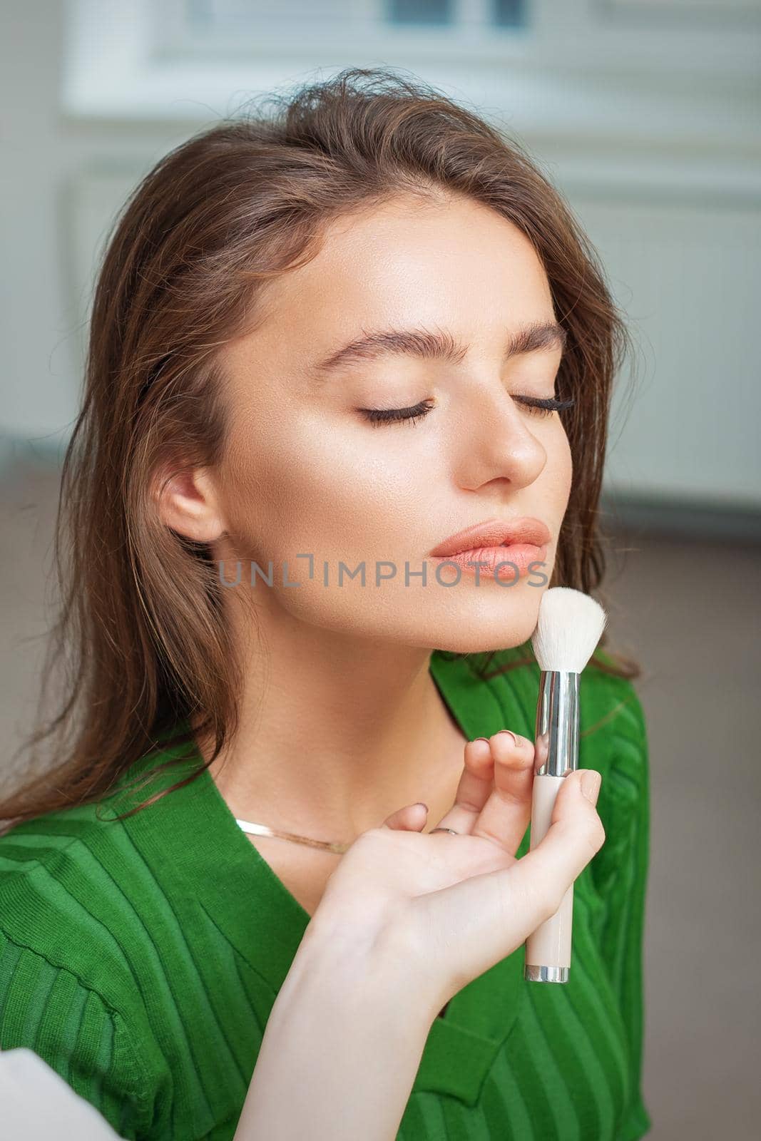 Make up artist applying professional make up of tonal foundation on the face of beautiful young caucasian woman in make up room. Base for make up.