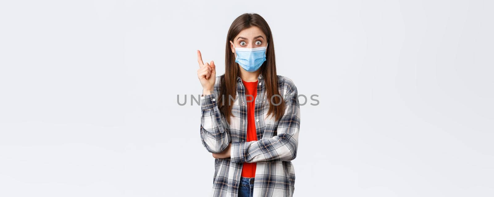 Coronavirus outbreak, leisure on quarantine, social distancing and emotions concept. Excited smart young woman in medical mask and checked shirt, raising index finger to say suggestion, have idea by Benzoix