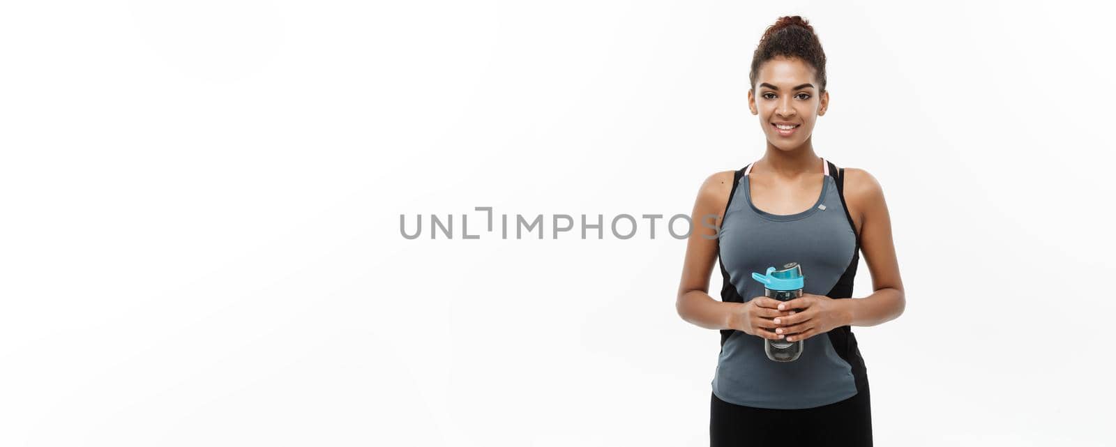 Healthy and Fitness concept - beautiful African American girl in sport clothes holding water bottle after workout. Isolated on white studio background by Benzoix